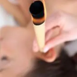 Kobieta leżąca na plecach podczas zabiegu z użyciem płonącej świecy w uchu, widok z góry, rozmyte tło.