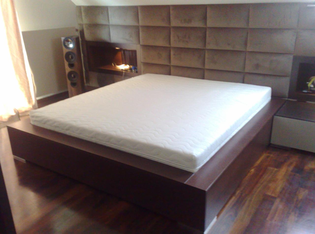 Nowoczesne łóżko z ciemnego drewna z tapicerowanym wezgłowiem w kwadraty, oświetlona półka w wezgłowiu, parkiet na podłodze.