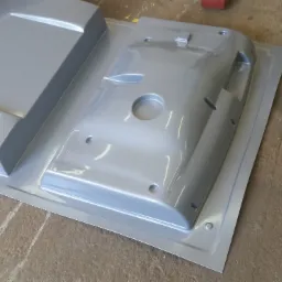 Dwa elementy metalowe, prawdopodobnie obudowy, po procesie spawania, pomalowane na srebrno, leżące na szarej powierzchni.