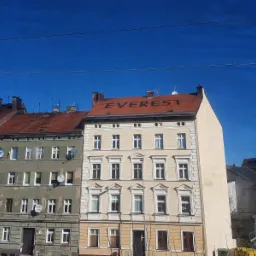 Kamienica z pomalowanym napisem 'EVEREST' na czerwonej dachówce, widok z ulicy w słoneczny dzień.