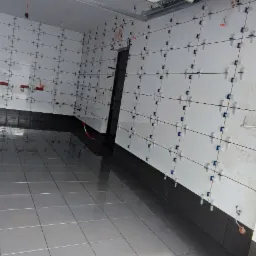 Proces układania białych płytek na ścianie z użyciem krzyżyków dystansowych i poziomego lasera, połączony z ułożeniem ciemnoszarych płytek podłogowych, widoczne wystające kable.