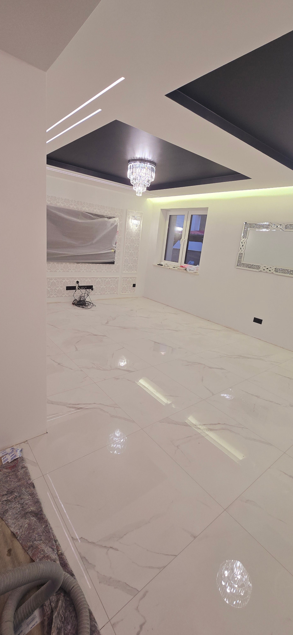 Eleganckie wykończenie salonu w Sośnie: białe płytki podłogowe z marmurowym wzorem, dekoracyjny sufit z oświetleniem LED i kryształowy żyrandol.