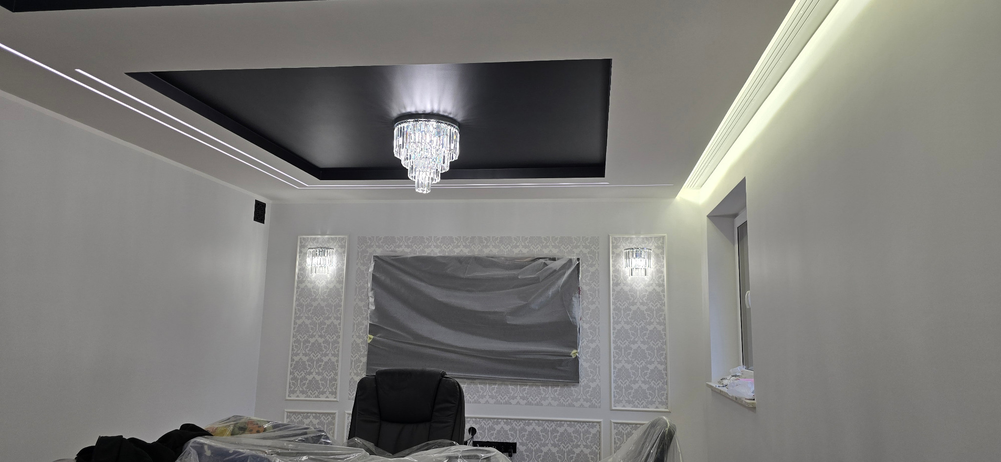 Nowoczesne wykończenie wnętrza: czarny sufit podwieszany z kryształowym żyrandolem i oświetleniem LED. Ściany białe z dekoracyjnymi panelami i wzorzystą tapetą.