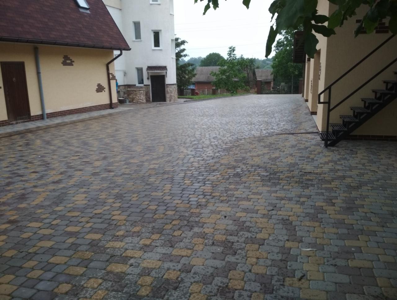 Ułożona kostka brukowa w odcieniach szarości i żółci na podjeździe między budynkami o elewacjach w kolorach beżu i bieli.