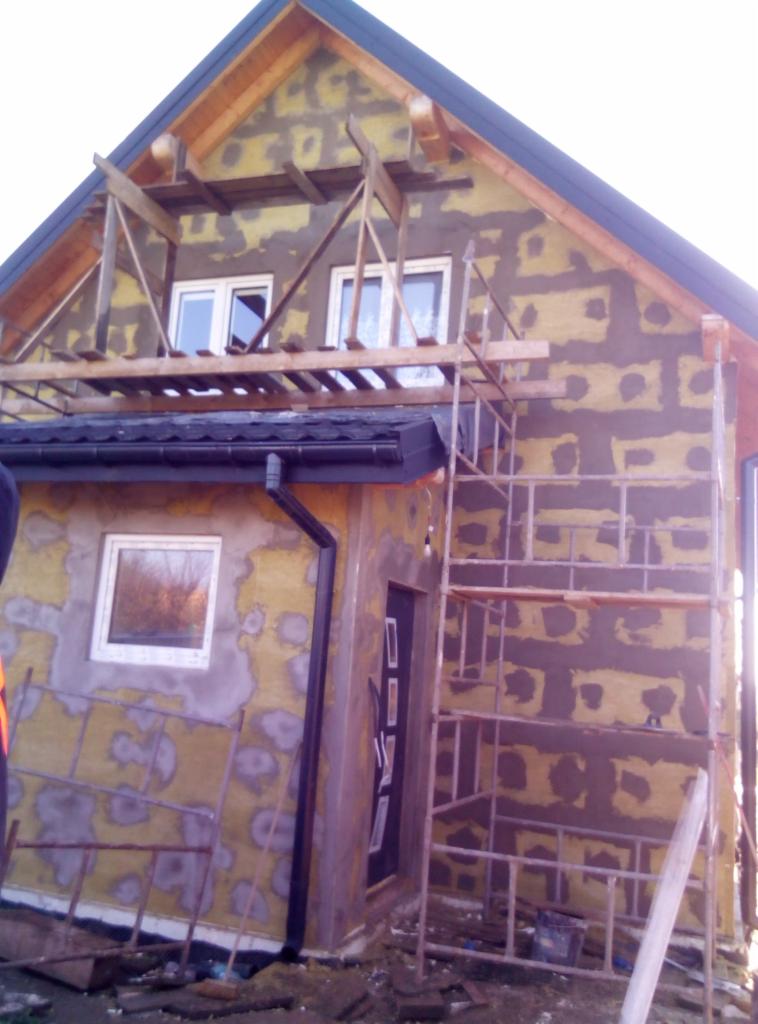 Dom w trakcie prac elewacyjnych w Krakowie: widoczne rusztowania, warstwa kleju z zatopioną siatką oraz częściowo ocieplona ściana z widocznymi fragmentami izolacji.