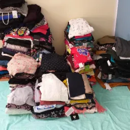 Dwie sterty posegregowanej odzieży na turkusowym ręczniku, widoczne metki i różne wzory tkanin, w rogu pokoju.