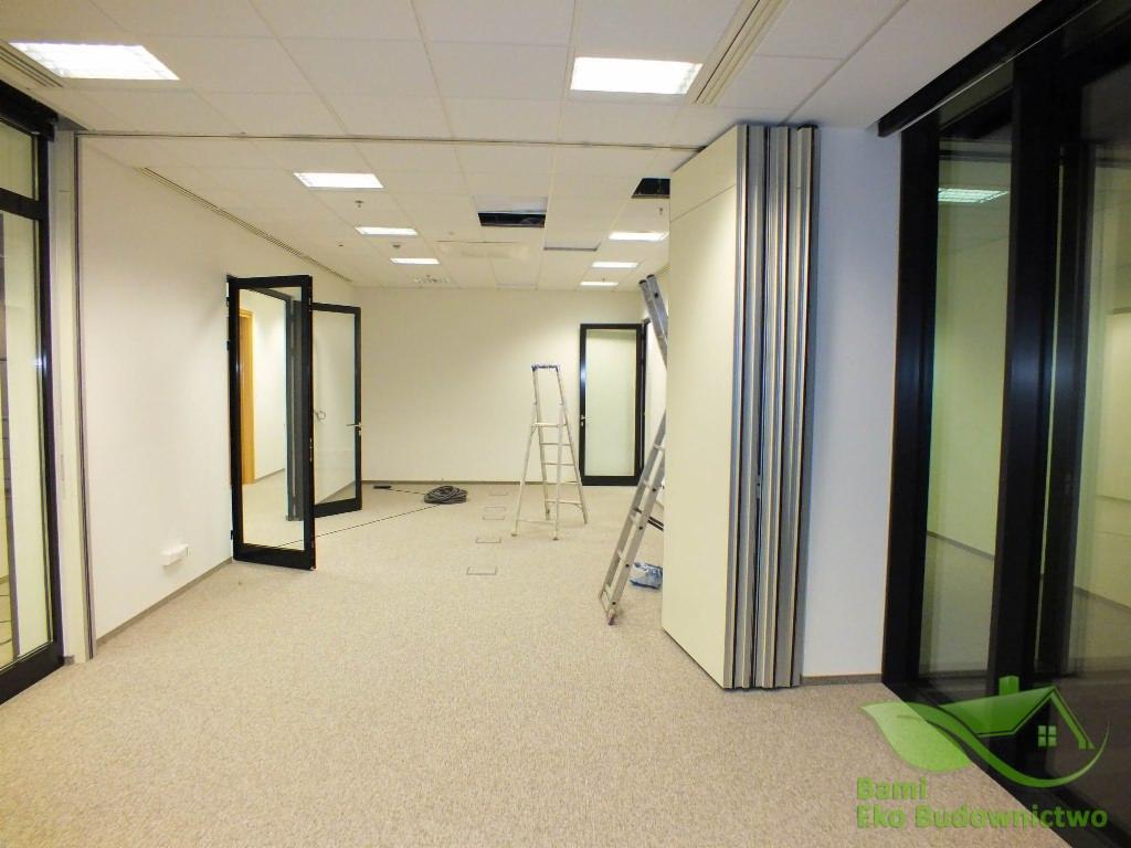 Wnętrze biura w Rzeszowie w trakcie prac wykończeniowych, widoczne przesuwne ściany działowe, drabina i otwarte szklane drzwi.