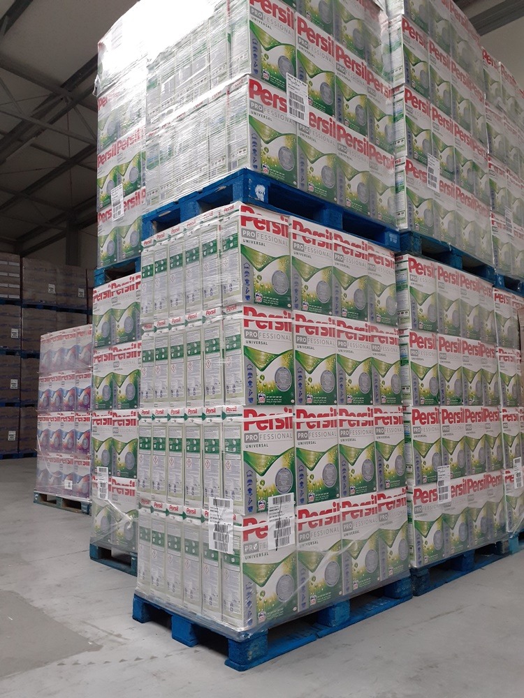 Palety z zapasem profesjonalnego środka czystości Persil Universal, składowane w magazynie z widocznymi stalowymi elementami konstrukcyjnymi.
