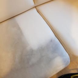 Clean Life Sp. z o.o. - Fragment jasnej kanapy z widoczną różnicą w czystości tapicerki po częściowym praniu, z ciemniejszą, zabrudzoną częścią po lewej stronie i czystą, jaśniejszą po prawej.