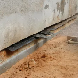 Fundament budynku z widoczną warstwą hydroizolacji i podkładkami dystansowymi, przygotowywany do dalszych prac, z narzędziami obok.