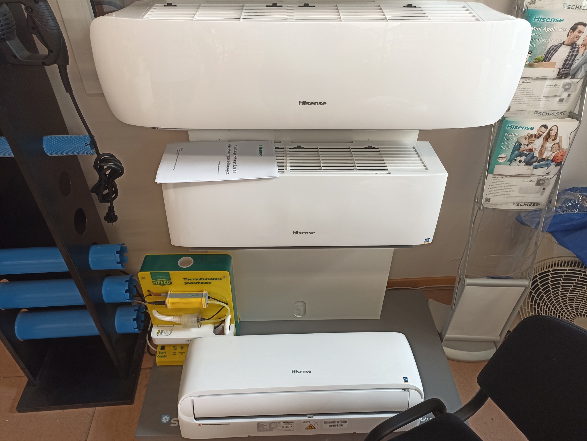 Trzy jednostki wewnętrzne klimatyzacji Hisense ustawione jedna nad drugą w pomieszczeniu, obok narzędzi i materiałów reklamowych.
