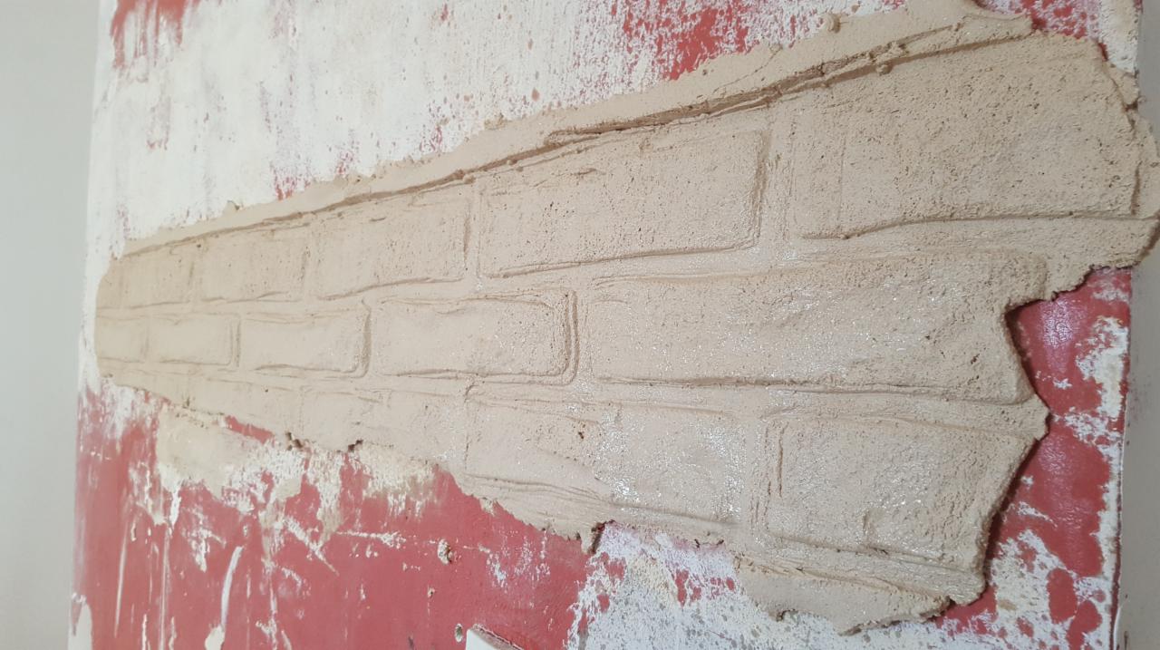 Fragment ściany z nałożoną fakturą imitującą cegłę, widoczne niedociągnięcia i pozostałości farby na ścianie.