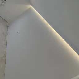 Biała ściana pod skosem z oknem dachowym i subtelnym oświetleniem LED wzdłuż krawędzi, fragment surowej ściany po lewej stronie.