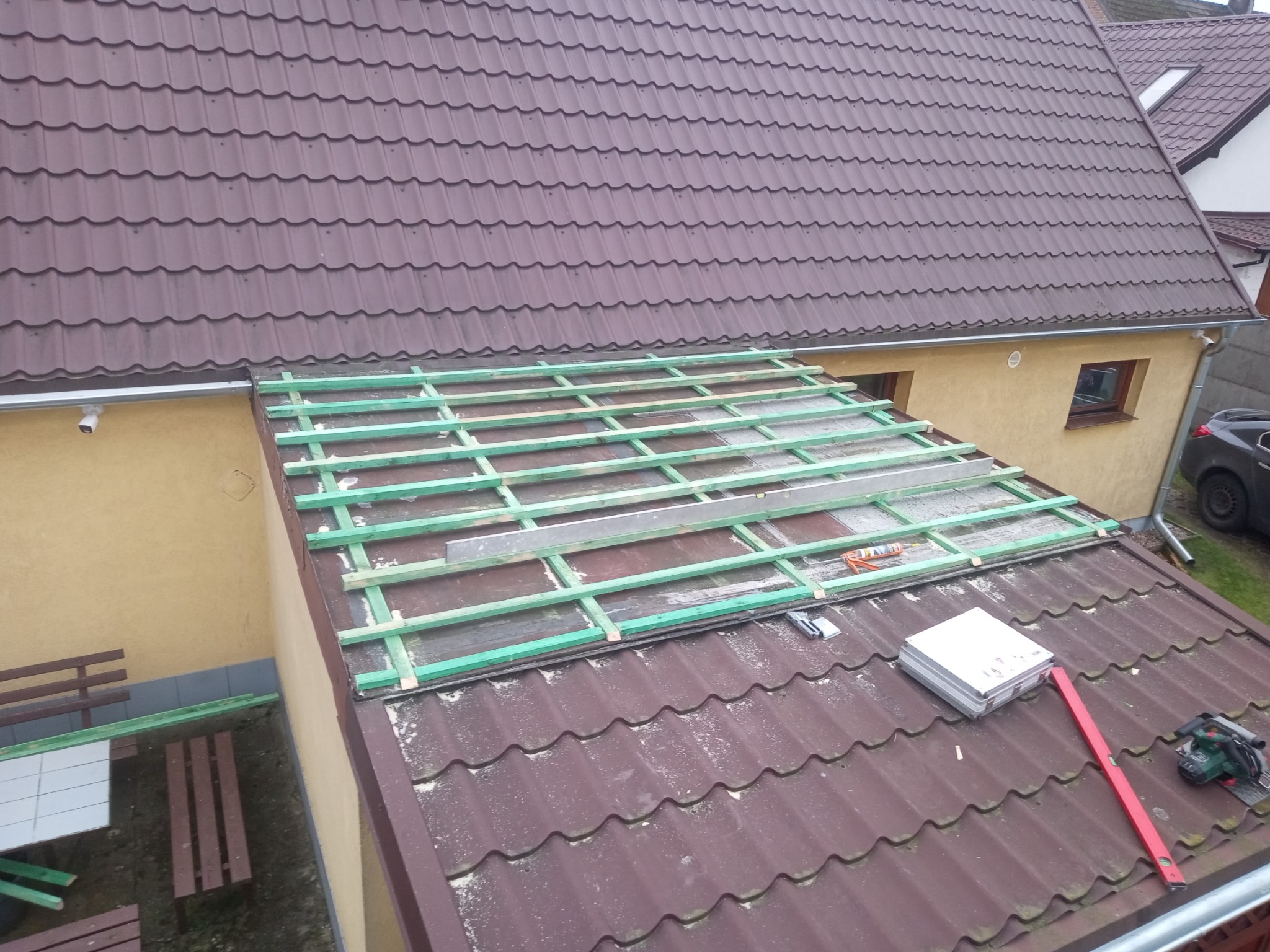 Montaż konstrukcji drewnianej na dachu pokrytym brązową dachówką, widoczne narzędzia, poziomica i skrzynka narzędziowa.