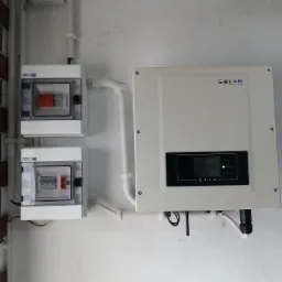 Biały inwerter solarny marki Sofar zamontowany na ścianie, z dwoma skrzynkami bezpiecznikowymi poniżej, połączone białymi rurami PCV.