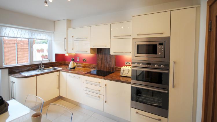 Jasna kuchnia z kremowymi szafkami, blatem z brązowego marmuru i sprzętem AGD ze stali nierdzewnej, widoczny czajnik i toster.