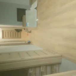 Jasne panele podłogowe ułożone wzdłuż długiego korytarza z widocznymi drzwiami z jasnego drewna i dekoracyjnymi wstawkami.