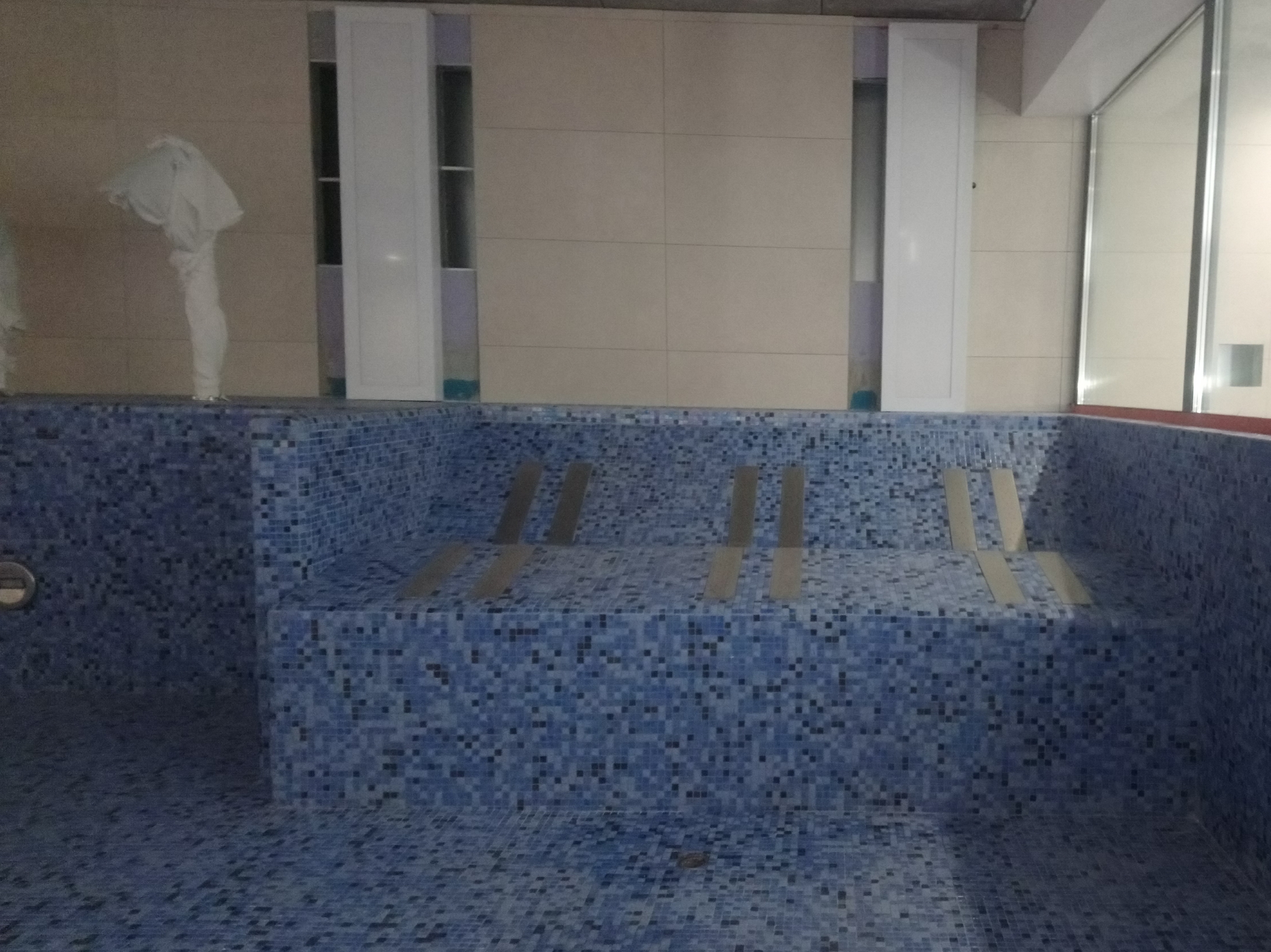 Niebieska mozaika w nieukończonym basenie, z metalowymi listwami dystansowymi, widoczne płytki ścienne i zabudowy w tle.