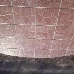 Kafelkowana powierzchnia z wzorem imitującym kamień, ułożona w siatkę z jasnymi fugami, widoczna z perspektywy od dołu, z fragmentem zewnętrznego otoczenia w dolnej części kadru.