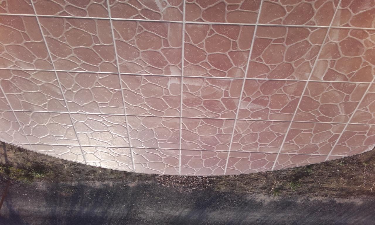 Kafelkowana powierzchnia z wzorem imitującym kamień, ułożona w siatkę z jasnymi fugami, widoczna z perspektywy od dołu, z fragmentem zewnętrznego otoczenia w dolnej części kadru.