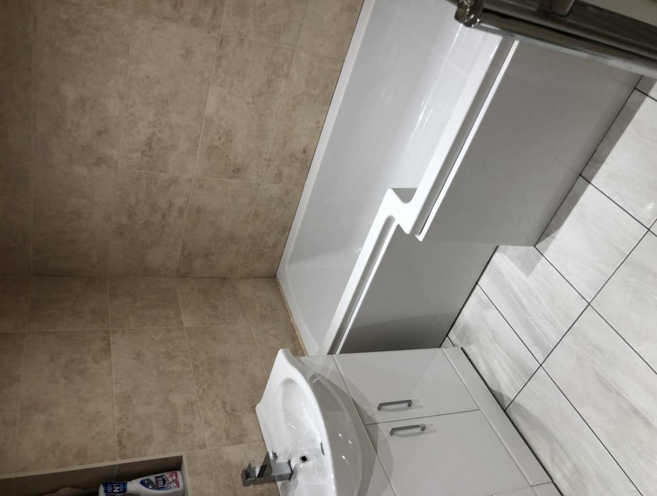 Wykończona łazienka z beżowymi płytkami ściennymi, białą wanną z asymetrycznym kształtem, białą szafką pod umywalką i szarymi płytkami podłogowymi.