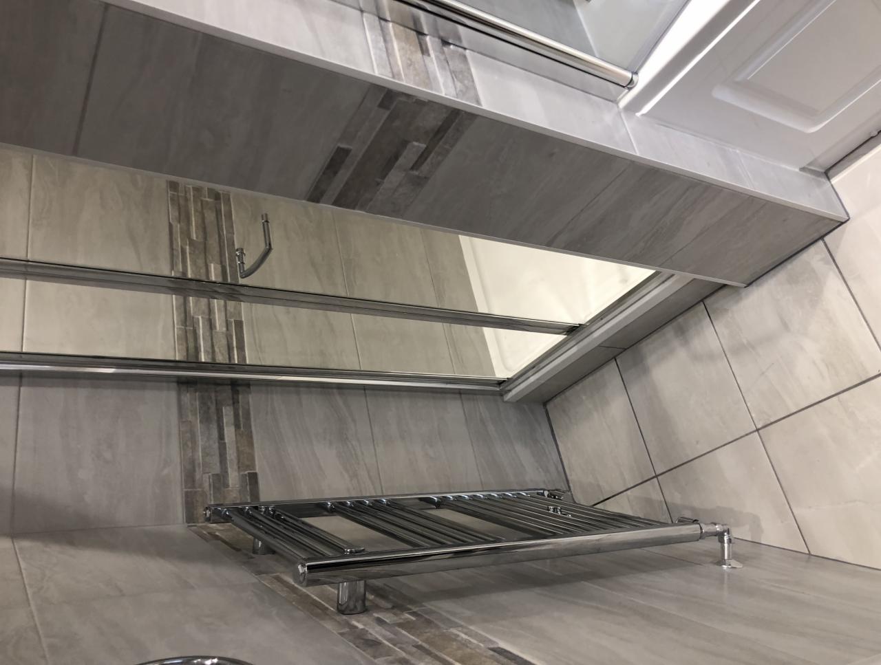 Szara łazienka z chromowanym grzejnikiem drabinkowym i dekoracyjnymi wstawkami z mozaiki na ścianach.