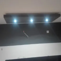 Wykończone wnętrze z czarno-białymi ścianami, podwieszanym sufitem z trzema punktowymi lampami LED i wystającym przewodem elektrycznym.