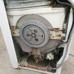 Wnętrze zdemontowanej zmywarki z widocznymi śladami rdzy na elementach metalowych i obudowie, ukazujące jej mechanizmy.