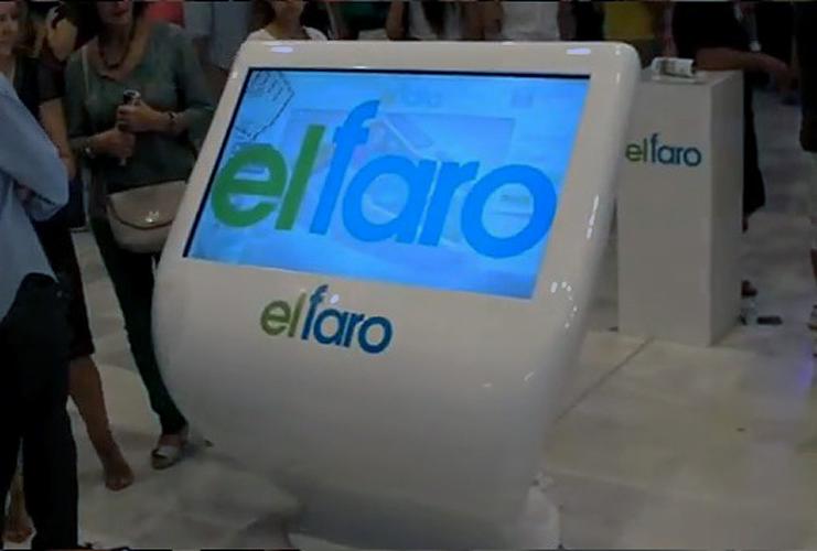 Biały kiosk interaktywny z logo 'elfaro' na ekranie i obudowie, otoczony przez ludzi w tle. Nowoczesny design, jasne oświetlenie, eventowa atmosfera.