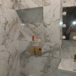 TP-BUD - Wykończona łazienka z marmurowymi płytkami, podświetlanym lustrem i zabudowaną toaletą. Widoczny fragment instalacji i akcesoria, tworzące elegancki i nowoczesny wystrój.