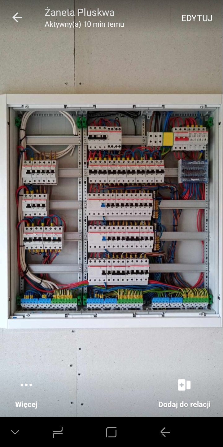 Rozdzielnica elektryczna w białej obudowie, widoczne liczne bezpieczniki, przewody i złączki. Instalacja schludna, z użyciem listew montażowych i oznaczeń kolorystycznych.