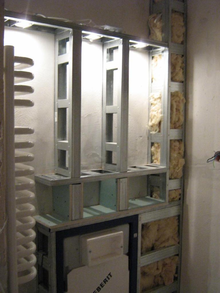 Konstrukcja stelaża z profili metalowych pod zabudowę wnęki w łazience, widoczna izolacja z wełny mineralnej, rura odpływowa i częściowo zamontowany stelaż podtynkowy Geberit.