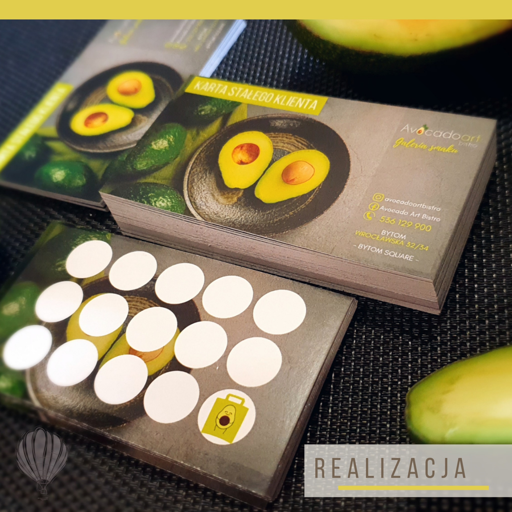 Stos kart lojalnościowych dla Avocadart Bistro, z grafiką przedstawiającą przekrojone awokado na talerzu, na dolnej karcie widoczne naklejone białe pola do zbierania punktów, w tle połówki awokado.