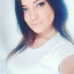 Portret kobiety z długimi, ciemnymi włosami i jasną cerą, ubrana w białą koszulkę, z delikatnym uśmiechem.