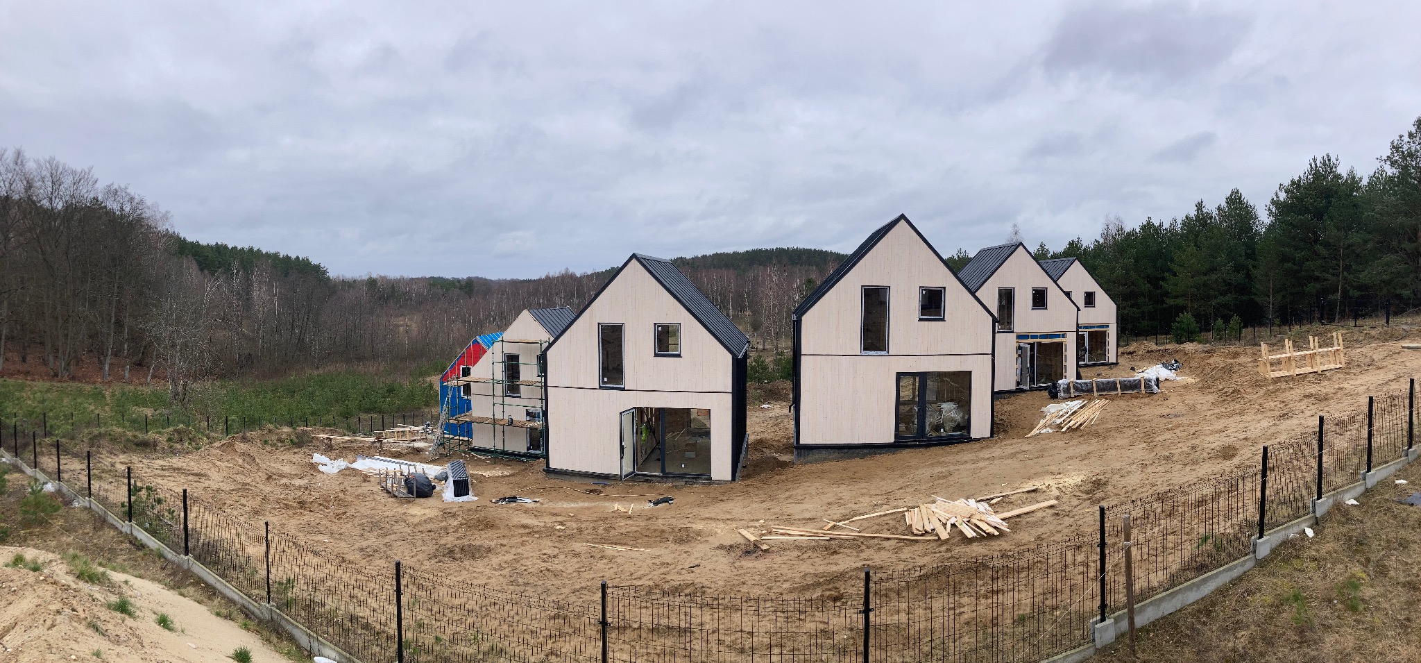 Panorama z budowy osiedla domów jednorodzinnych z drewnianą elewacją, widoczne rusztowania i teren przygotowany pod zagospodarowanie.