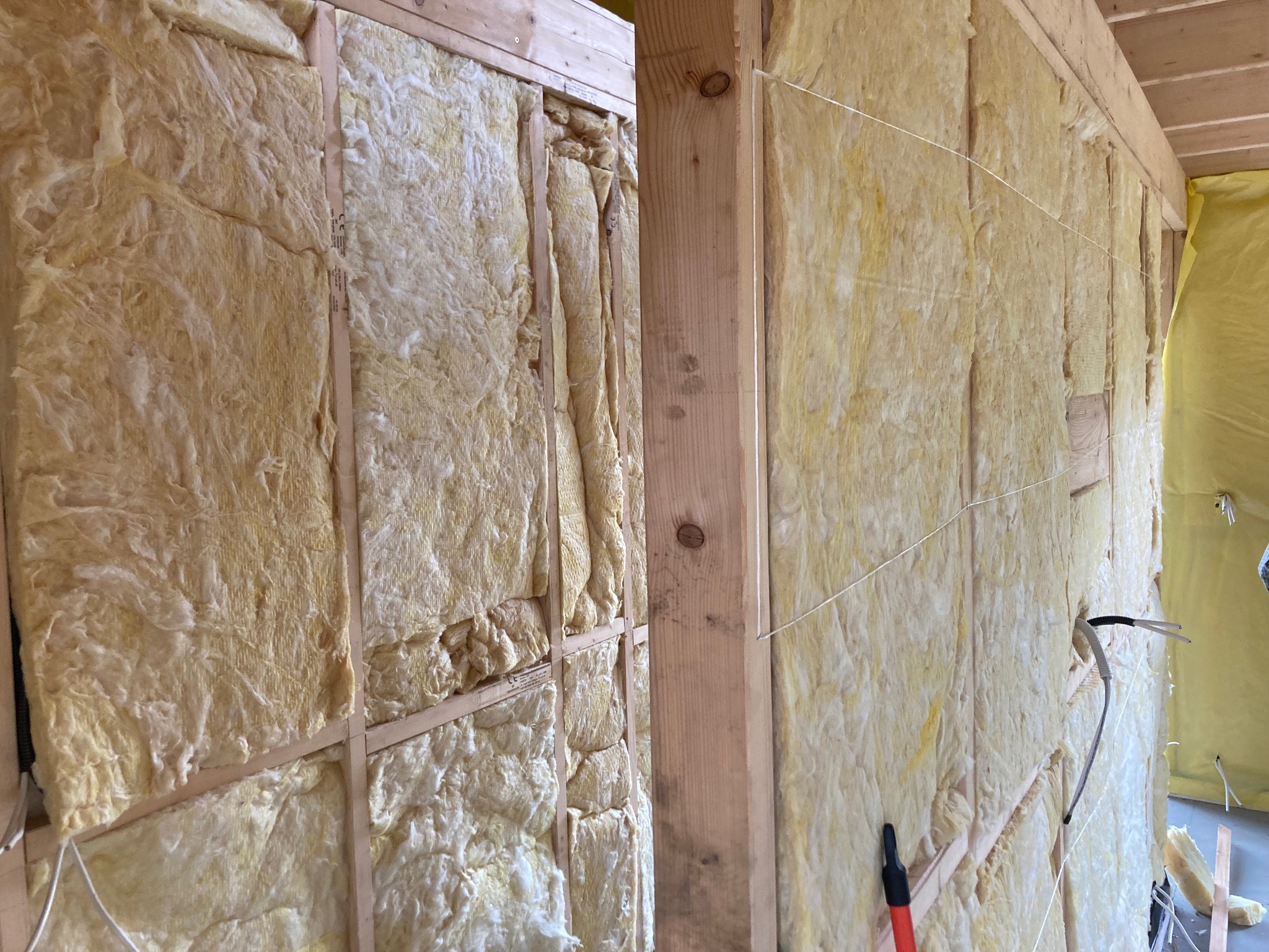 Wnętrze ściany szkieletowej z izolacją z wełny mineralnej, widoczne drewniane belki i przewody elektryczne.