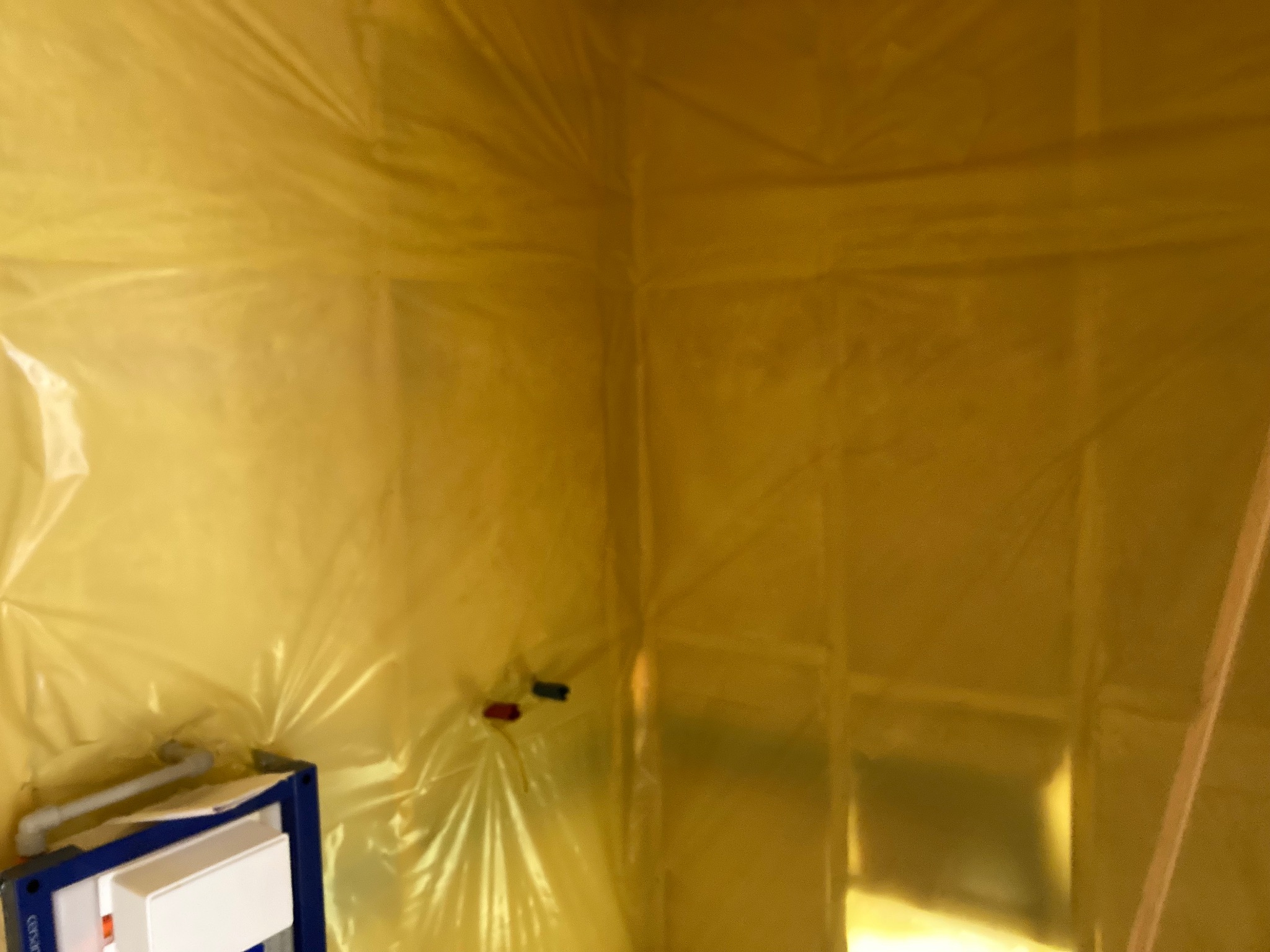 Przygotowanie łazienki do remontu: ściany i sufit zabezpieczone folią malarską, widoczny stelaż podtynkowy WC.