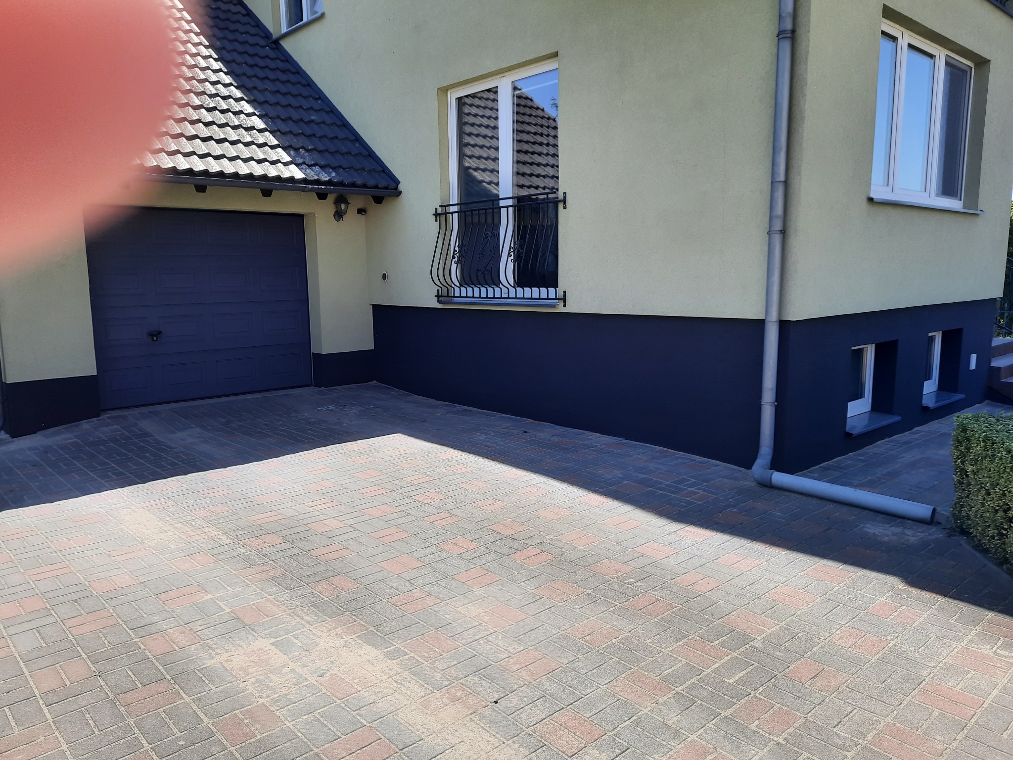 Jasnożółty dom z ciemnoniebieskim garażem i cokołem, widok z zewnątrz na kostkę brukową, okno z ozdobną balustradą.