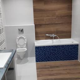 CLEAN MASTER BY TRUST TREE - Nowoczesna łazienka w trakcie wykańczania, z brązowymi płytkami imitującymi drewno na ścianie i podłodze, białą armaturą i wanną obłożoną mozaiką w odcieniach niebieskiego, widoczne niedokończone...