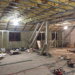 CLEAN MASTER BY TRUST TREE - Poddasze w trakcie adaptacji: izolacja wełną mineralną w metalowym stelażu, widoczne okna, rusztowania i narzędzia, bałagan na podłodze.