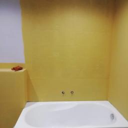 CLEAN MASTER BY TRUST TREE - Biała wanna w trakcie montażu w łazience z żółtymi ścianami przygotowanymi pod płytki; widoczne niezabezpieczone przyłącza wodne i częściowo pomalowana ściana.