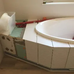 Montaż płytek z wzorem na obudowie wanny, widoczne krzyżyki dystansowe, poziomica i pojemnik z narzędziami.