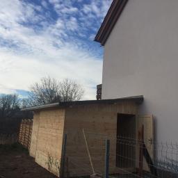 CLEAN MASTER BY TRUST TREE - Nowo wybudowana drewniana szopa ogrodowa z otwartymi drzwiami, przylegająca do ściany domu, widoczna siatka ogrodzeniowa i dekoracyjny płotek.