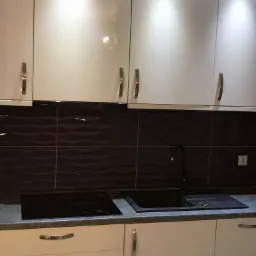 Nowoczesna kuchnia w Ełku z białymi, lakierowanymi szafkami, ciemnobrązowymi płytkami z falistym wzorem i czarną armaturą.