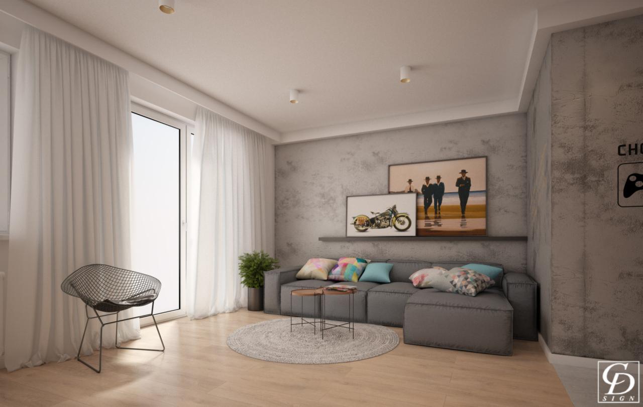 Nowoczesny salon z szarą sofą modułową, okrągłym dywanem i metalowym krzesłem, ozdobiony obrazami motocykla i postaci na plaży, z akcentem rośliny doniczkowej przy oknie.