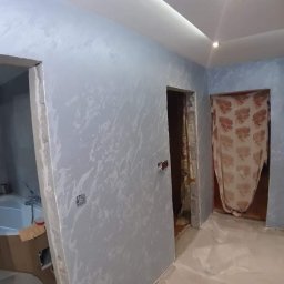 Dariusz - Pokój po odświeżeniu ścian z dekoracyjną fakturą w odcieniach szarości i błękitu, widoczna łazienka w trakcie prac wykończeniowych oraz zabezpieczona folią podłoga.