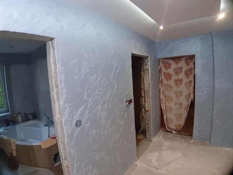 Pokój po odświeżeniu ścian z dekoracyjną fakturą w odcieniach szarości i błękitu, widoczna łazienka w trakcie prac wykończeniowych oraz zabezpieczona folią podłoga.