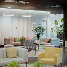 Hol wejściowy biura w stylu retro: pastelowe sofy, geometryczny stolik kawowy, rośliny doniczkowe i oświetlenie dyskowe.