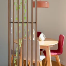 Drewniana ażurowa ścianka działowa z pnącą rośliną, okrągły stół z krzesłami w odcieniach bieli i czerwieni, ceramiczne wazony, lampa wisząca w kolorze koralowym, fragment szarej sofy w tle.