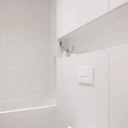 Minimalistyczna, całkowicie biała łazienka z geometryczną mozaiką na ścianie nad wanną, wiszącą szafką i toaletą z ukrytym systemem spłukiwania.